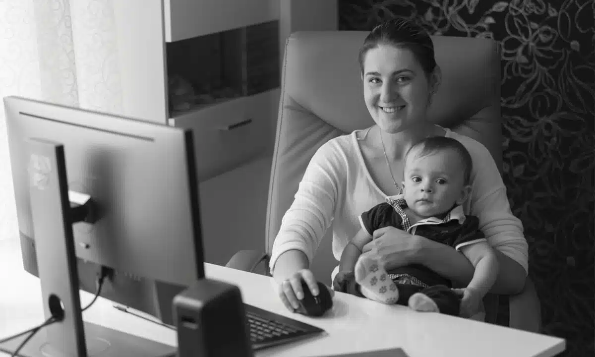 Une femme qui travaille devant son ordinateur avec son bébé dans les bras